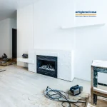 Soggiorno in ristrutturazione con camino rivestito in mattoni bianchi e focolare nero, a terra attrezzi e cavi da cantiere.