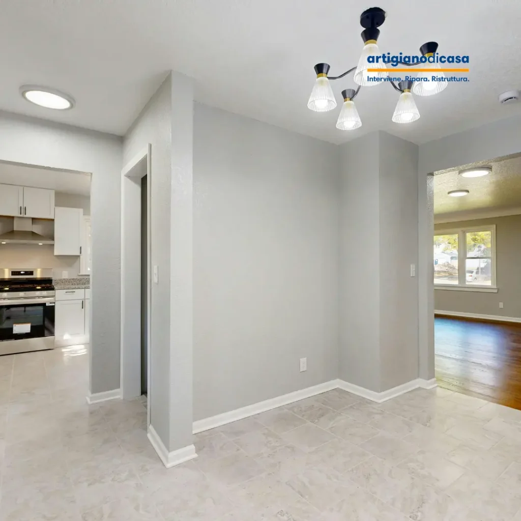 Interno ristrutturato con pareti grigie, pavimento in piastrelle e cucina a vista, illuminazione a soffitto e ambienti luminosi.